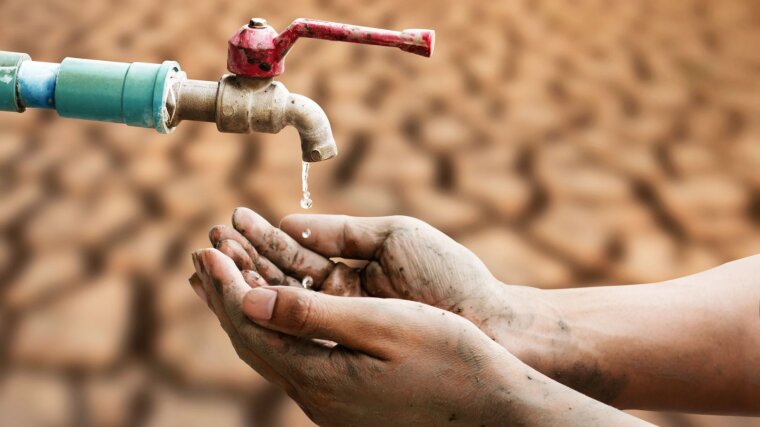Wassertropfen aus einem Wasserhahn tropfen vor einem vertrockneten Boden in menschliche Hände